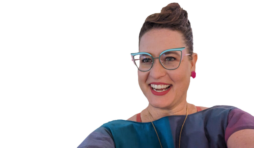 Smiling Amber Nicole Cannan with large light blue and pink large cat-eye glasses and hair in a french twist. The lipstick and earrings match perfectly and the dress, handmade by Amber Nicole, matches the earrings, glasses and lipstick perfectly.