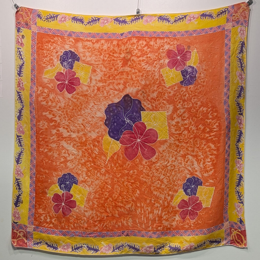 A large mostly orange silk scarf with hibiscus and Hawaiian glyphs.