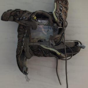 A pair of Oboz hiking shoes have been brutally cut in half and surrounding a 5x5 watercolor of a lovely tranquil water filled landscape. The shoes are worn, but still have lots of life left in them.